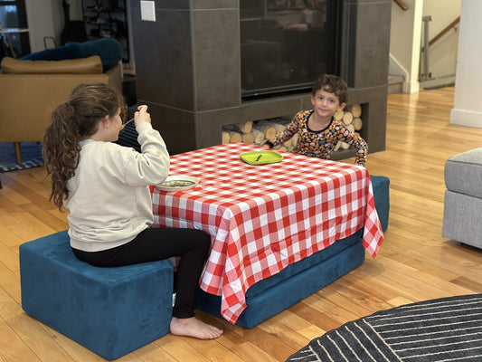 Two kids eating at a kids' Thanksgiving table built from stacked Figgy play couch cushions with a red gingham tablecloth