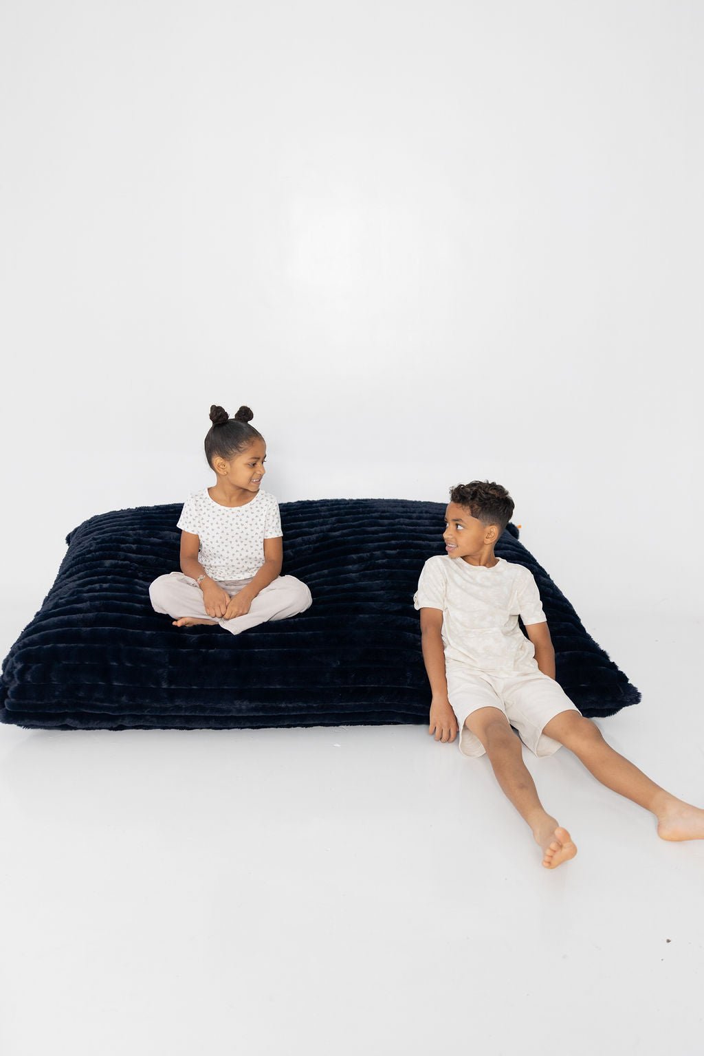 Two kids sitting on and beside a Night Owl Baggy